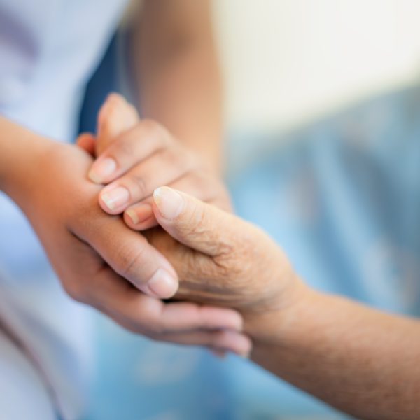 Nurse sitting on a hospital bed next to an older woman helping hands, care for the elderly concept